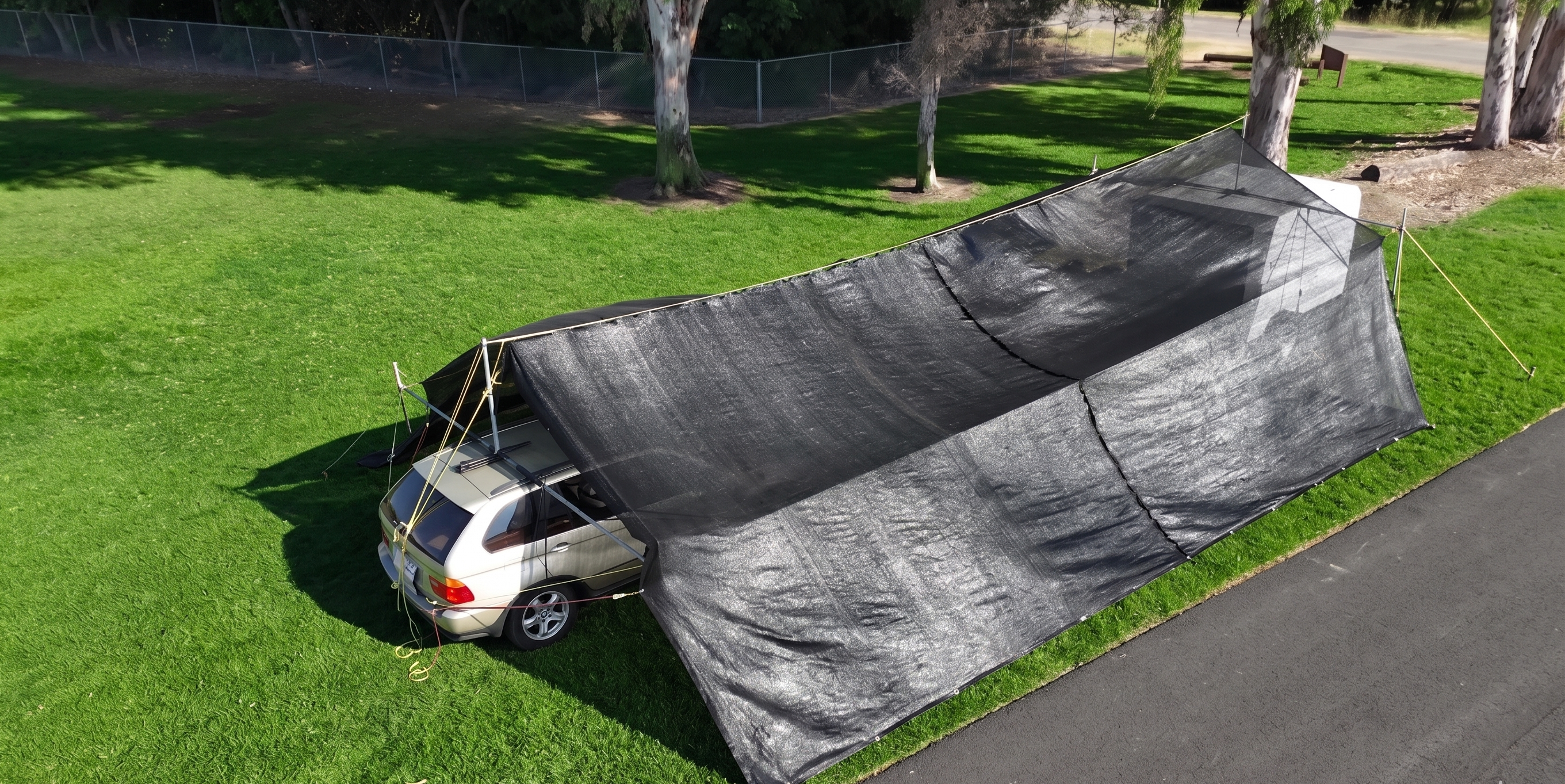 Car parked under a large black shade on a grassy area, hovershade SUV and trailer cabopy setup