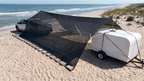 Car and trailer on a sandy beach with a large black shade sail attached to the hovershade frames anchored by the vehicles