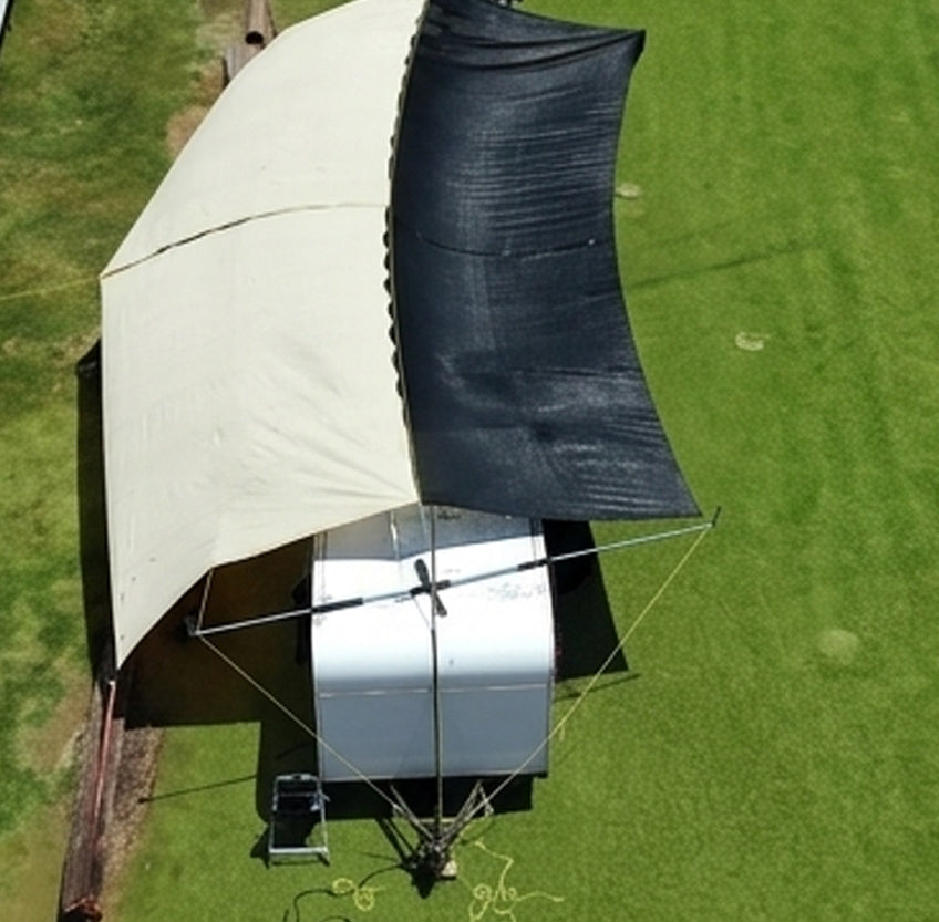 Shade structure set up on car and trailer as a sales tent on a grassy field with dual colored shade