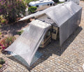 RV with extended hovershade silver shade awning parked on a paved area with trees and flowers in the background