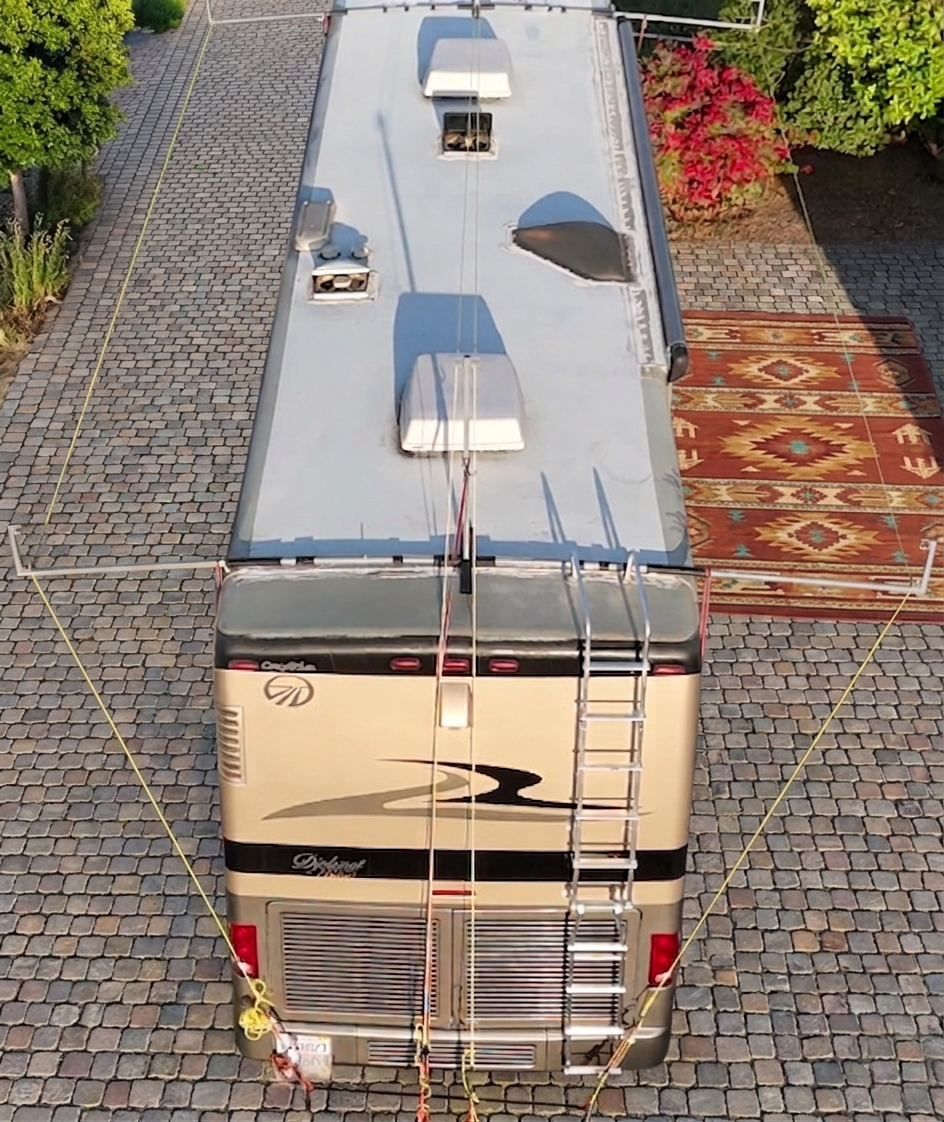 Large beige and black RV parked on a cobblestone street with hovershade frame attachment and lines connected to the vehicle without the shade fabric